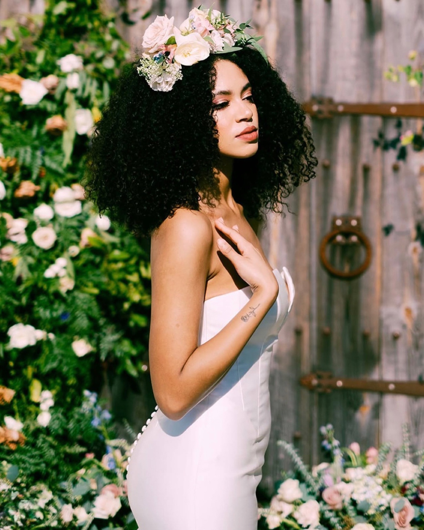 Bride with natural curls and a fresh flower crown against a rustic wooden door